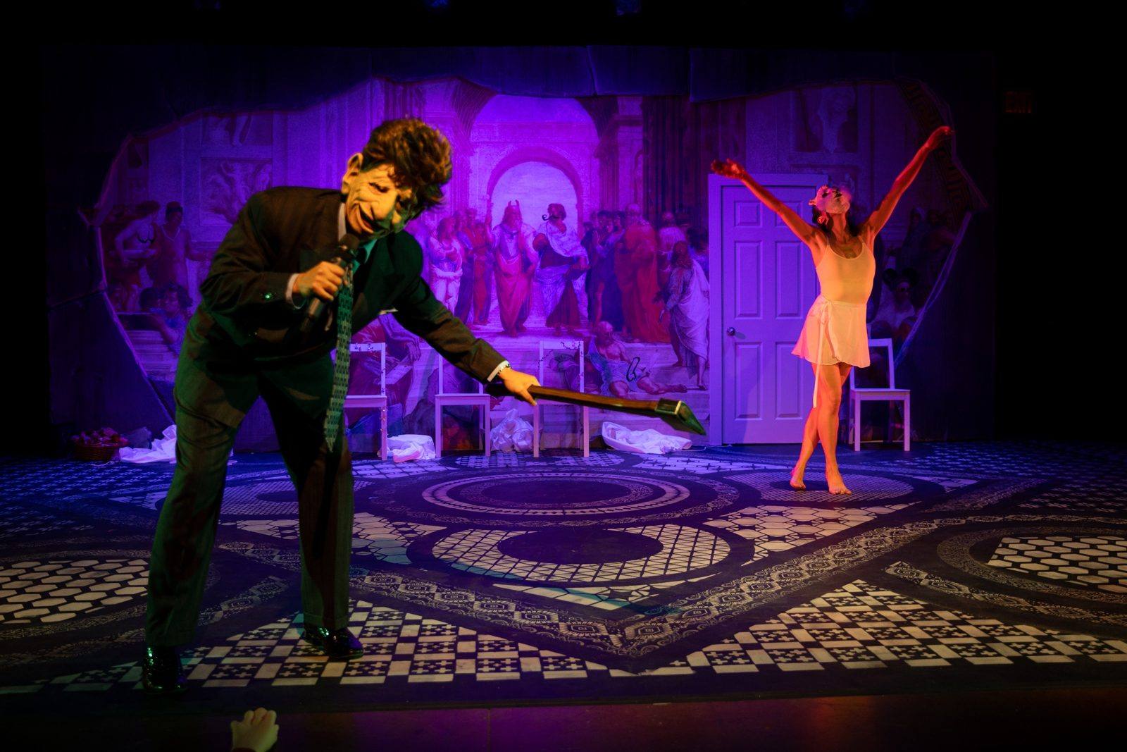 Aristotle Thinks Again: a masked man with a microphone and a dancer with arms raised before a School of Athens backdrop