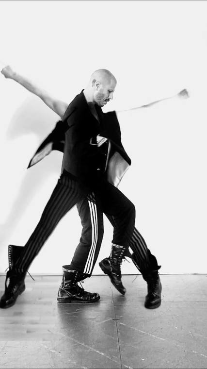 Communion: Dan Safer mid-step in black, a blurred double image of his arms and striped trousers trailing behind him