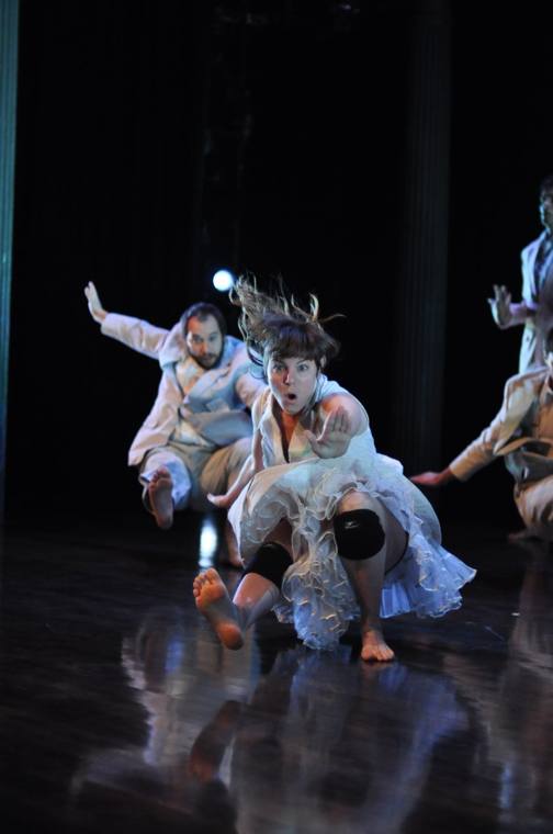 A dancer in a petticoat and knee pads slides toward the camera, mouth open
