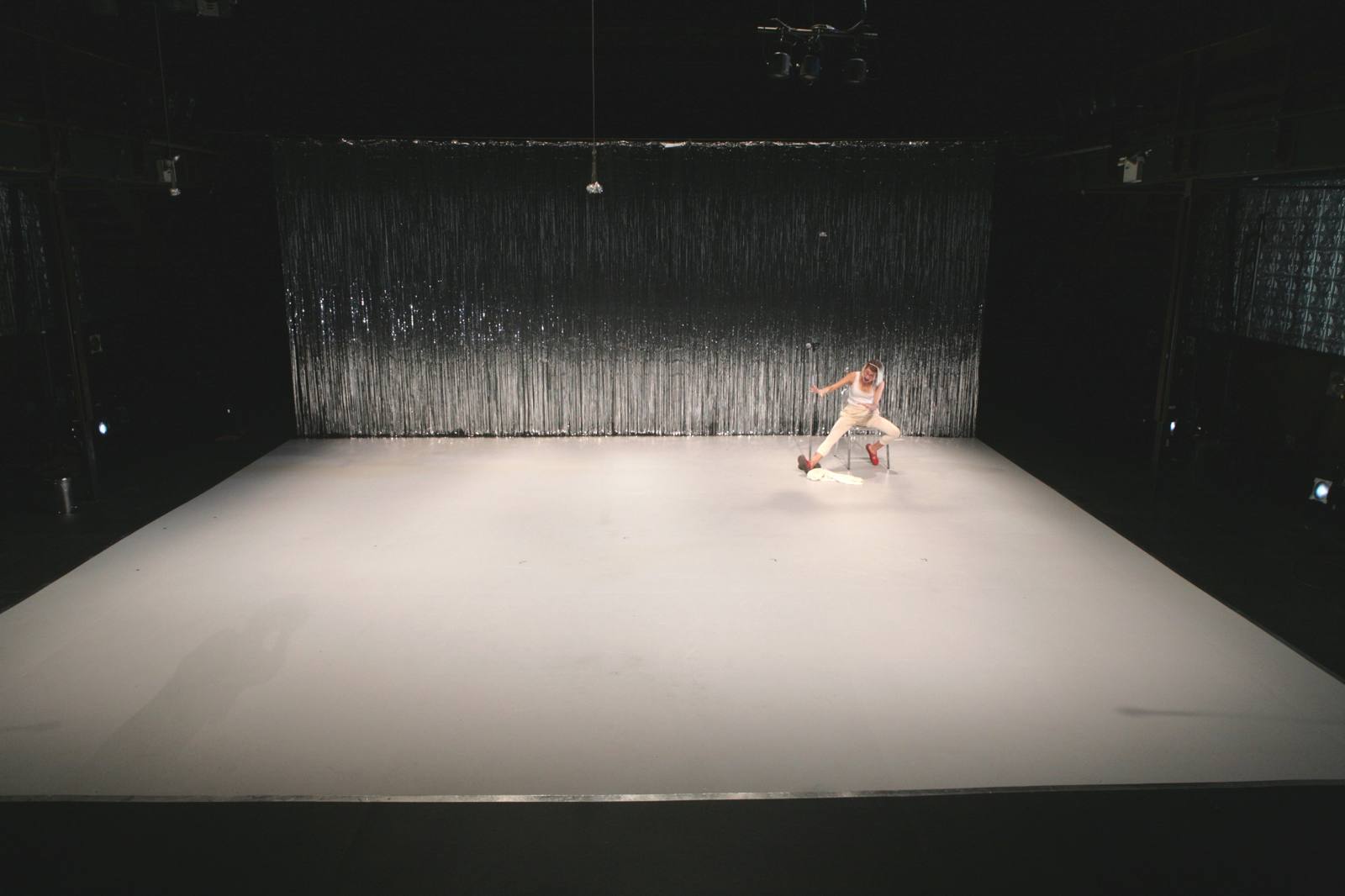 Five Days in March: a lone performer at the edge of a huge white floor before a tinsel curtain